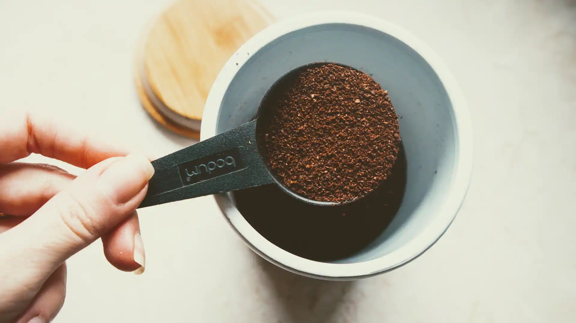 A hand holding a scoop full of coffee grounds over an open canister.