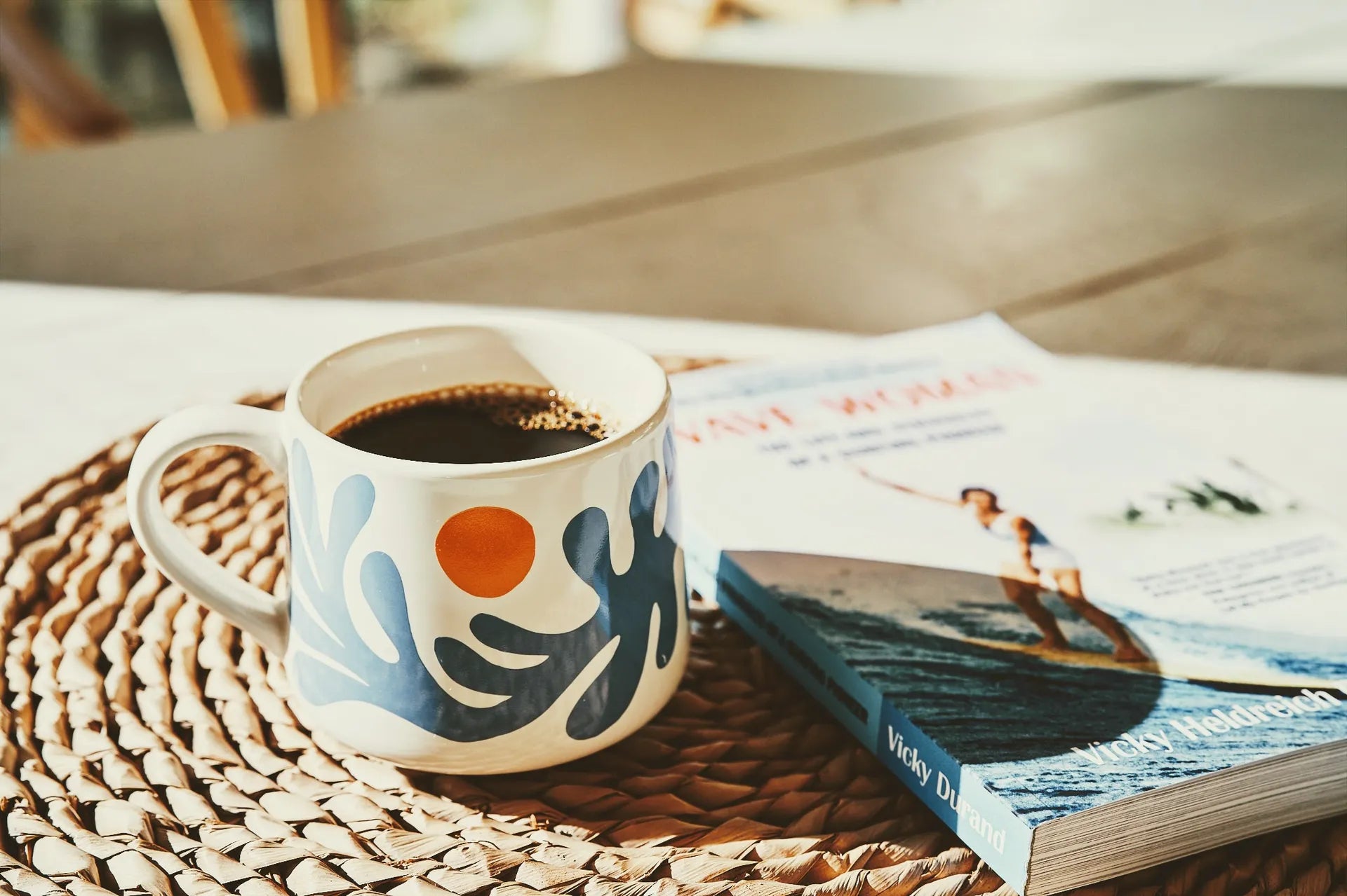 Laka Java coffee in a colorful mug on a grass mat next to a book about surfing.