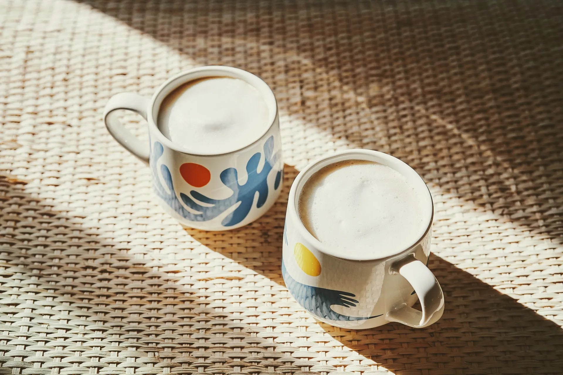 Two Laka Java lattes in colorful mugs on a grass mat.