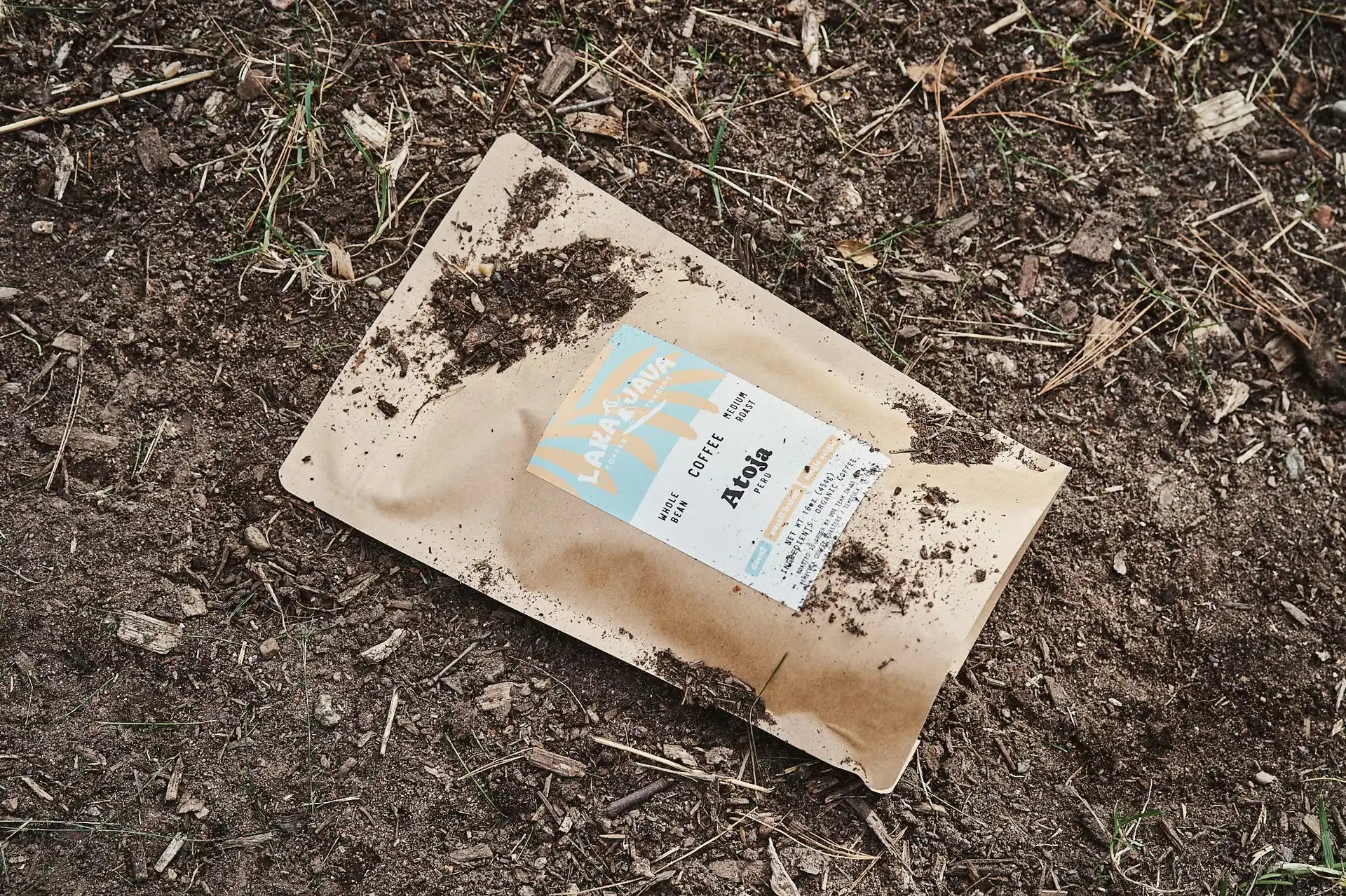 A bag of Laka Java Atoja decaf coffee beans on the ground with dirt on it.