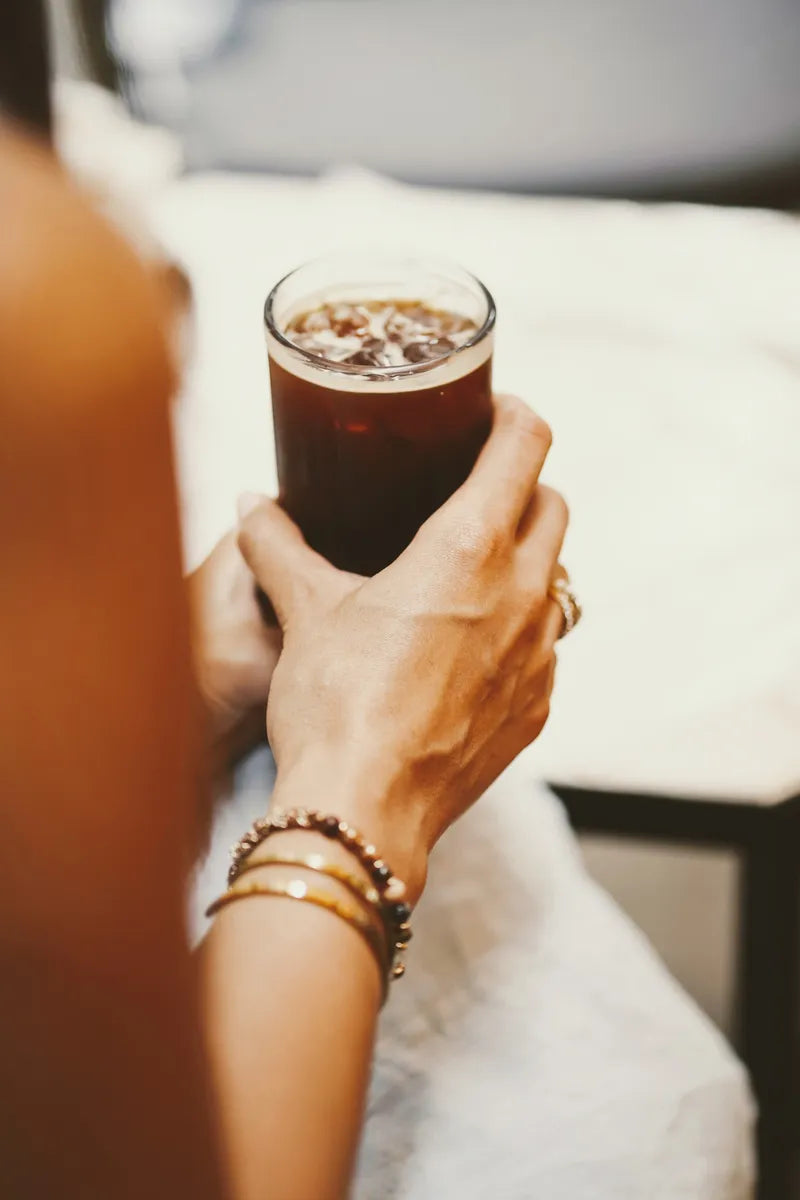 Hands holding a tall glass of cold brew coffee on ice in a cafe.