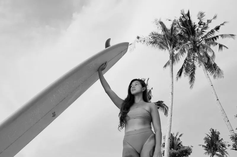 A woman in a bikini holding a surfboard up with one hand at the beach.